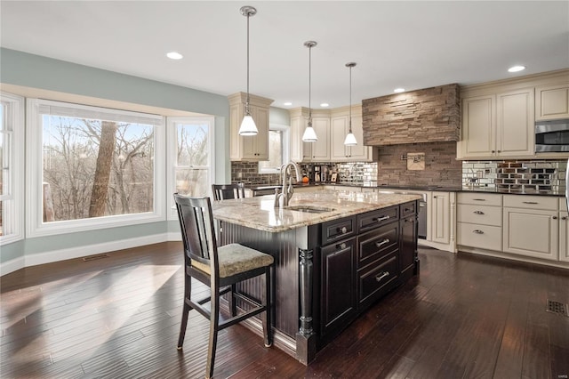 kitchen featuring sink, hanging light fixtures, dark stone countertops, a kitchen island with sink, and decorative backsplash