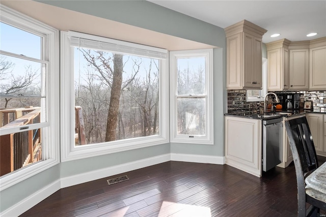 kitchen with sink, backsplash, dark hardwood / wood-style flooring, stainless steel dishwasher, and cream cabinetry