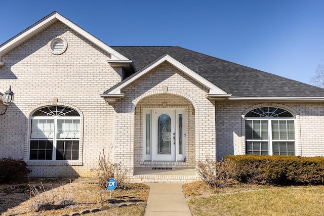 entrance to property with brick siding and roof with shingles