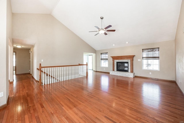 unfurnished living room with high vaulted ceiling, a ceiling fan, baseboards, a brick fireplace, and light wood finished floors