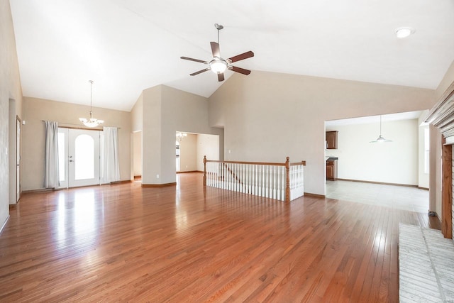 unfurnished living room with high vaulted ceiling, ceiling fan with notable chandelier, a fireplace, baseboards, and light wood-type flooring