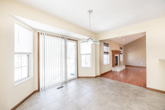 unfurnished room featuring a brick fireplace, plenty of natural light, visible vents, and baseboards