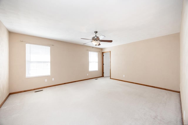 spare room with ceiling fan, light carpet, visible vents, and baseboards