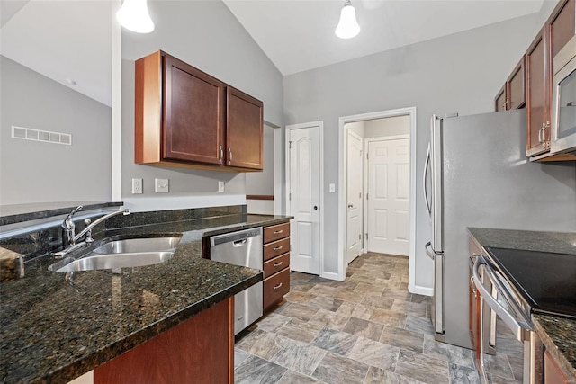 kitchen with lofted ceiling, sink, decorative light fixtures, appliances with stainless steel finishes, and dark stone counters