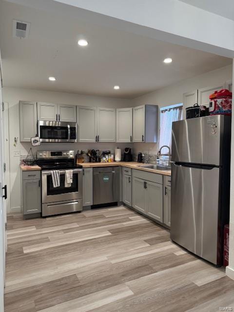 kitchen with gray cabinetry, sink, light wood-type flooring, and appliances with stainless steel finishes