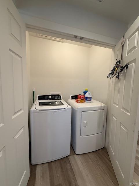 clothes washing area with washing machine and dryer and light hardwood / wood-style flooring