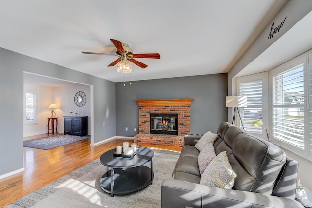 living room with ceiling fan, a brick fireplace, a healthy amount of sunlight, and light hardwood / wood-style floors