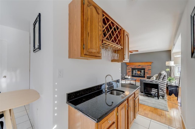 kitchen featuring light tile patterned flooring, dark stone counters, sink, and a brick fireplace