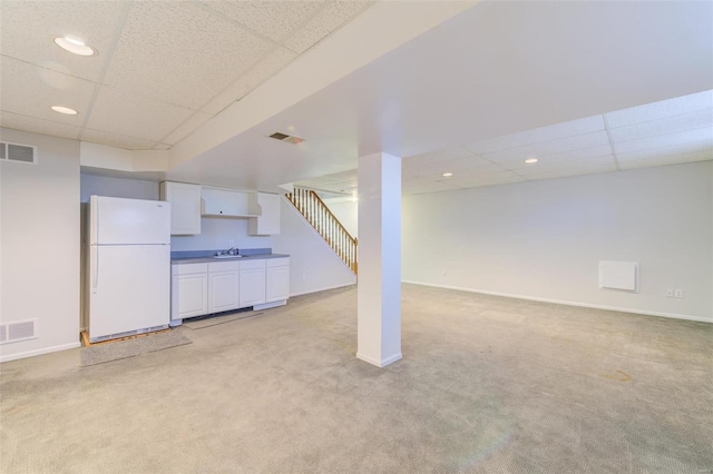 basement featuring white refrigerator, light colored carpet, sink, and a drop ceiling