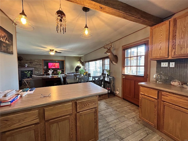 kitchen with pendant lighting, ceiling fan, beam ceiling, light hardwood / wood-style floors, and a stone fireplace