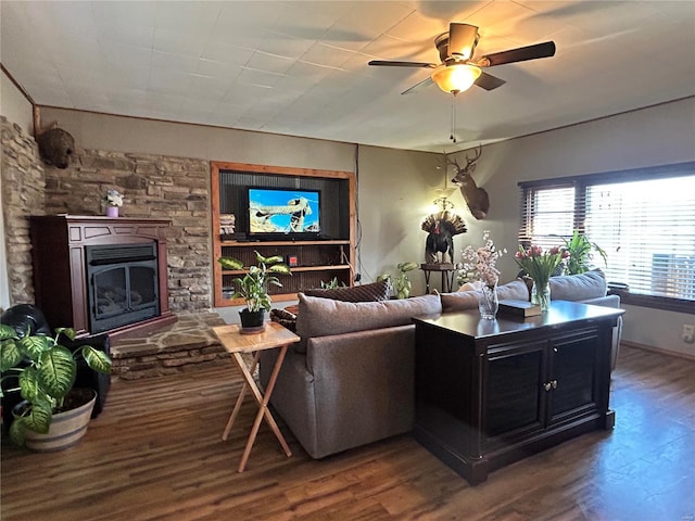 living room featuring ceiling fan, dark hardwood / wood-style floors, and a stone fireplace