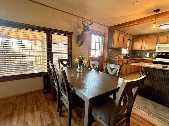 dining room featuring sink, light hardwood / wood-style flooring, and beamed ceiling