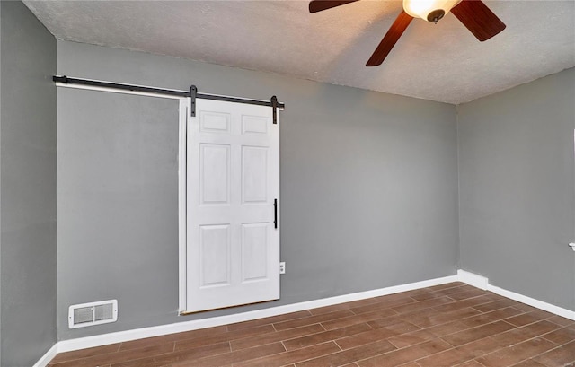 empty room featuring a barn door, a textured ceiling, and ceiling fan