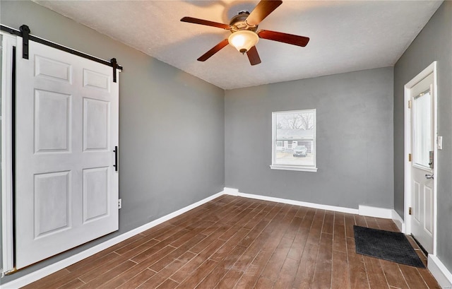 entryway with a barn door, dark wood-type flooring, and ceiling fan