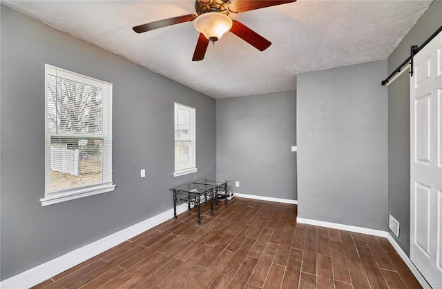 spare room featuring ceiling fan, a barn door, a textured ceiling, and dark hardwood / wood-style flooring