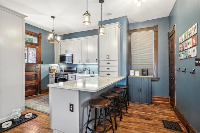 kitchen with hanging light fixtures, white cabinetry, appliances with stainless steel finishes, and light stone countertops