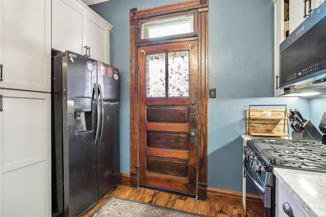 kitchen with stainless steel appliances, white cabinetry, and light hardwood / wood-style flooring