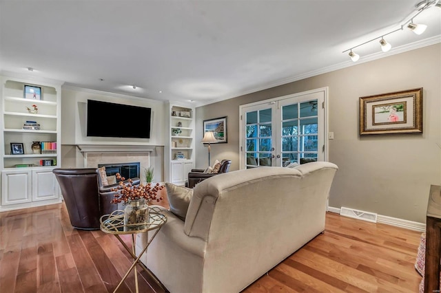 living room featuring french doors, a fireplace, light hardwood / wood-style floors, and crown molding