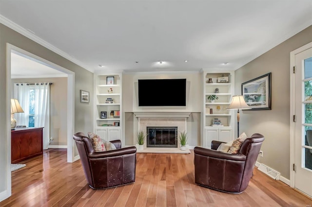 living room with built in shelves, ornamental molding, and light wood-type flooring