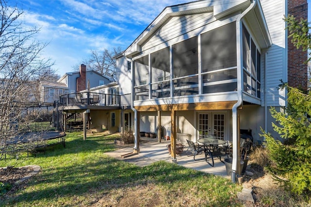 back of property featuring french doors, a trampoline, a lawn, a patio, and a sunroom