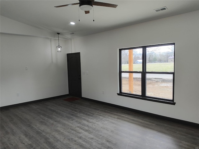 empty room featuring dark wood-style floors, a ceiling fan, visible vents, and baseboards