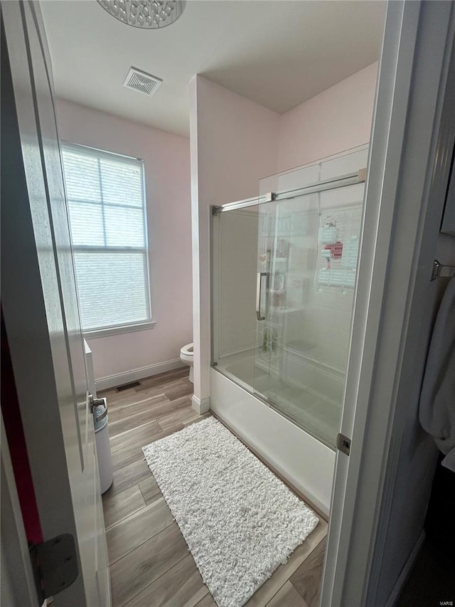 bathroom with hardwood / wood-style floors, shower / bath combination with glass door, and toilet