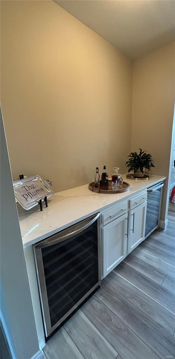 bar with sink, light hardwood / wood-style flooring, stainless steel dishwasher, beverage cooler, and white cabinets