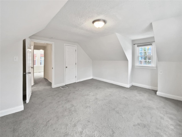 additional living space featuring lofted ceiling, dark carpet, and a textured ceiling