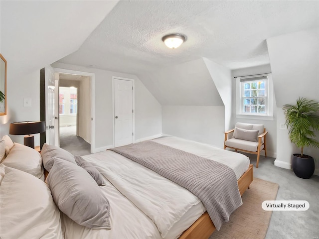 bedroom with lofted ceiling, light colored carpet, and a textured ceiling