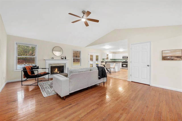 living area featuring a premium fireplace, light wood-type flooring, a ceiling fan, and baseboards