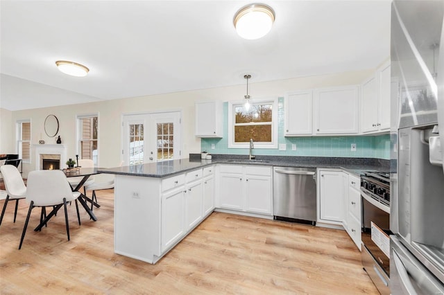 kitchen featuring a warm lit fireplace, stainless steel appliances, a peninsula, a sink, and light wood-type flooring