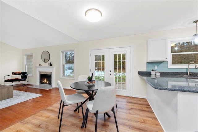 dining space featuring french doors, a fireplace, lofted ceiling, light wood-type flooring, and baseboards