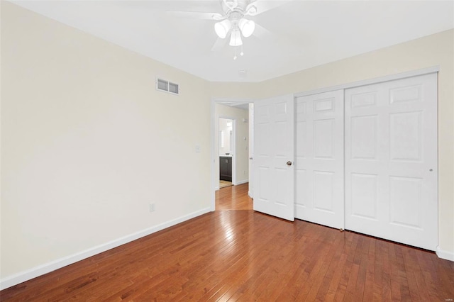 unfurnished bedroom with a closet, wood-type flooring, visible vents, ceiling fan, and baseboards