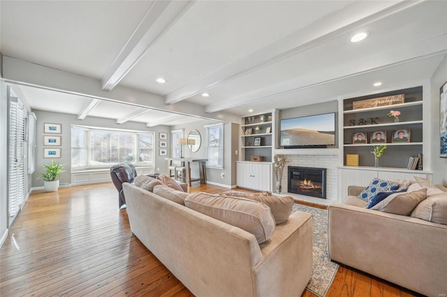 living room with beamed ceiling, a fireplace, light wood-type flooring, and built in shelves