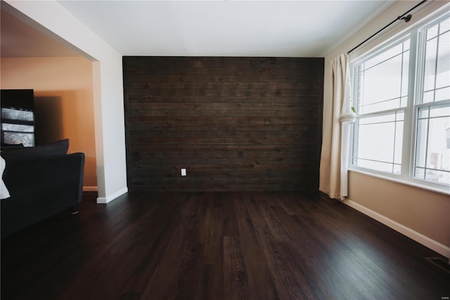 unfurnished room featuring a healthy amount of sunlight, dark hardwood / wood-style floors, and wood walls