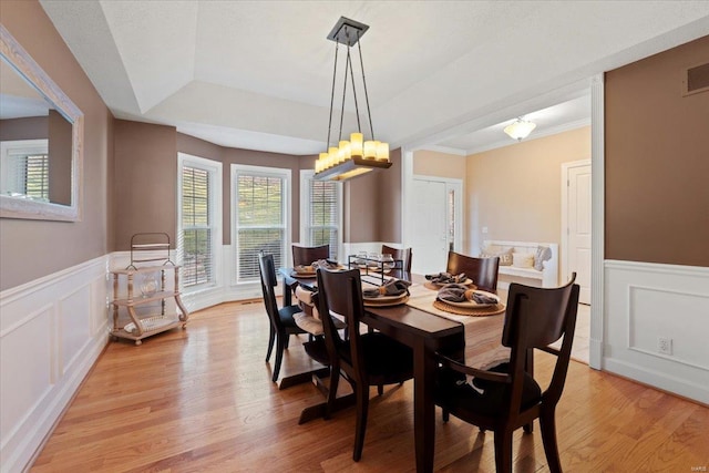 dining area with a wainscoted wall, a tray ceiling, a decorative wall, and light wood-style floors