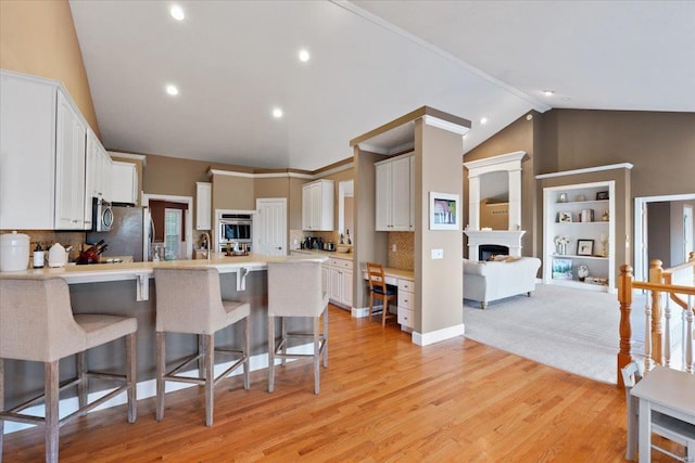 kitchen featuring a peninsula, a fireplace, white cabinets, a kitchen breakfast bar, and light countertops