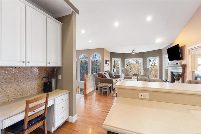 kitchen with white cabinets, light wood-style flooring, open floor plan, a fireplace, and backsplash