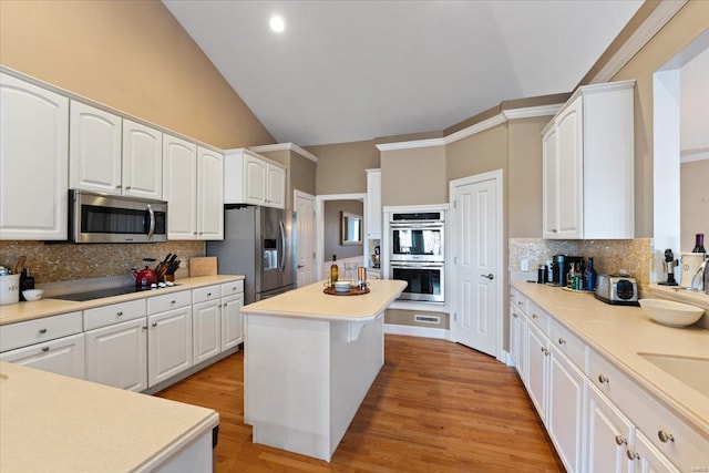 kitchen featuring lofted ceiling, a kitchen island, appliances with stainless steel finishes, light wood-type flooring, and white cabinetry