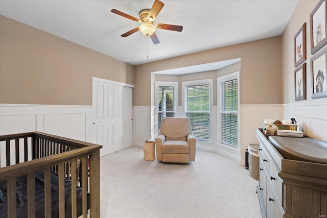 bedroom featuring light carpet, ceiling fan, a closet, and wainscoting