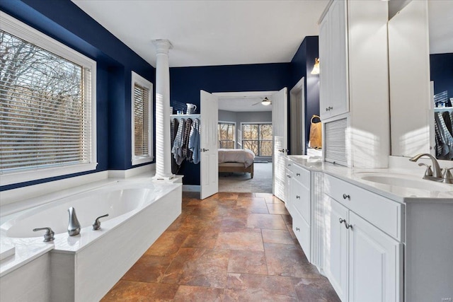 full bath featuring connected bathroom, a garden tub, stone finish flooring, vanity, and ornate columns