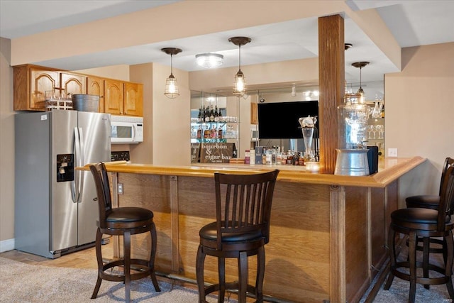 bar with hanging light fixtures, white microwave, stainless steel fridge, and indoor bar