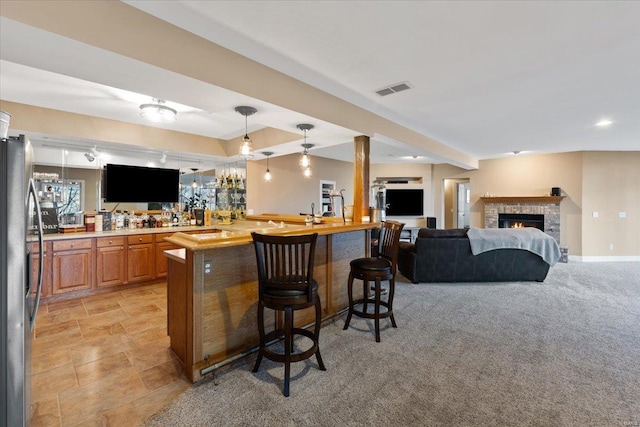 bar featuring visible vents, stainless steel fridge with ice dispenser, hanging light fixtures, a brick fireplace, and wet bar