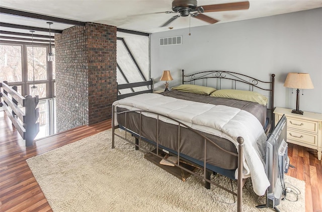 bedroom with visible vents, a ceiling fan, brick wall, wood finished floors, and beam ceiling