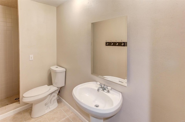 bathroom featuring baseboards, toilet, tile patterned floors, a shower stall, and a sink