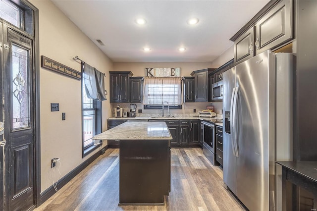 kitchen with sink, light stone counters, appliances with stainless steel finishes, a kitchen island, and hardwood / wood-style floors