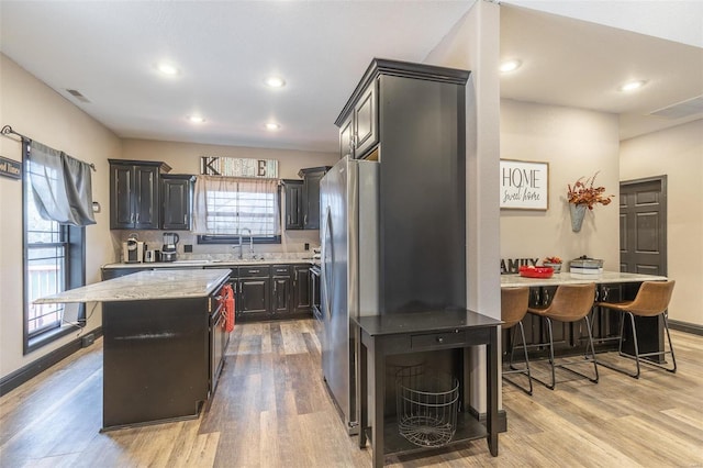 kitchen featuring sink, light hardwood / wood-style flooring, stainless steel fridge, a center island, and a kitchen bar