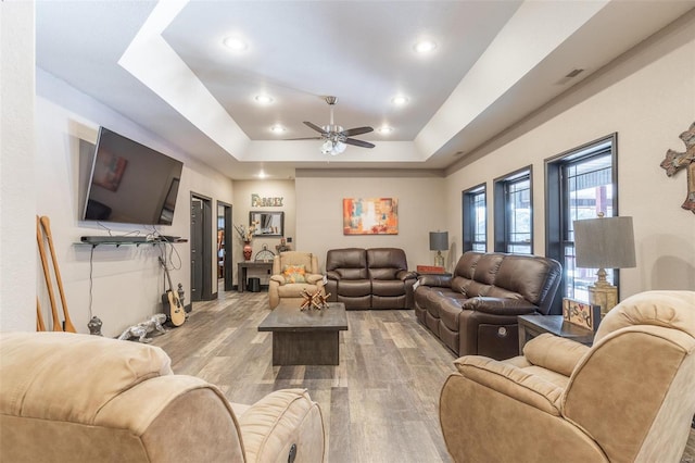 living room featuring ceiling fan, a raised ceiling, and light hardwood / wood-style floors