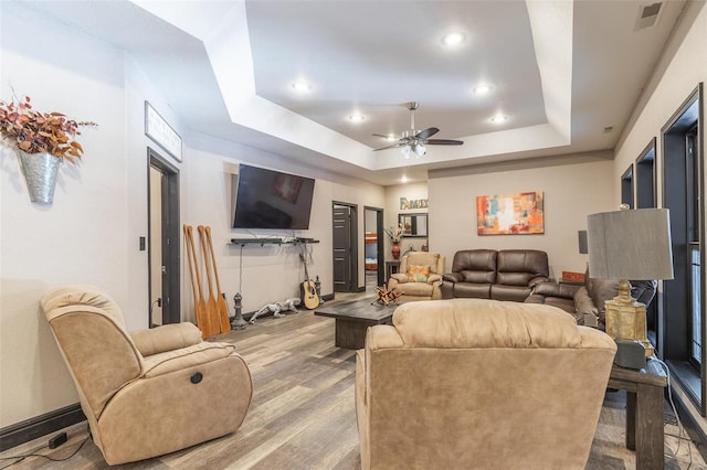 living room featuring a raised ceiling, ceiling fan, and light wood-type flooring