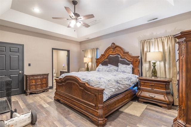 bedroom featuring ensuite bath, wood-type flooring, a raised ceiling, and ceiling fan